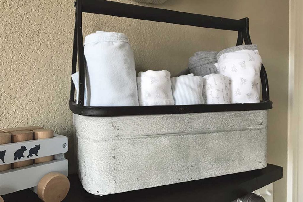 metal tool bin with burp cloths and blankets on top of DIY industrial pipe shelf in nursery