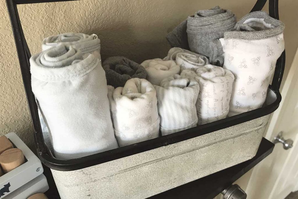 metal tool bin with burp cloths and blankets on top of DIY industrial pipe shelf in nursery