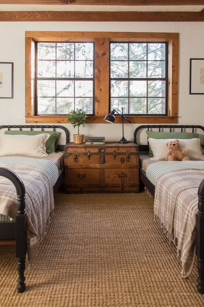 beautiful neutral children's room with antique steamer trunk, two Jenny Lind beds painted black, and natural wood window trim