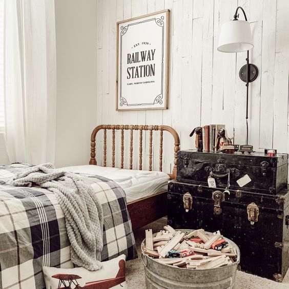 railway station boys bedroom with medium stained antique Jenny Lind bed, steamer trunks, wood toy train, and white vertical shiplap wall