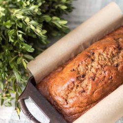 banana bread in cast iron loaf pan lined with parchment paper and boxwood wreath behind