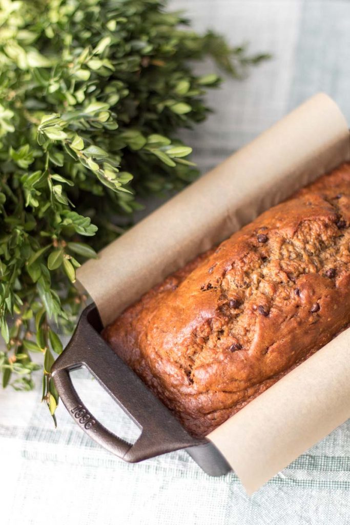 homemade einkorn banana bread in cast iron loaf pan lined with parchment paper and boxwood wreath behind