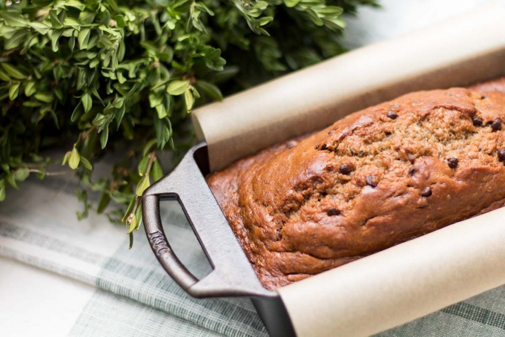 banana bread in cast iron loaf pan lined with parchment paper and boxwood wreath behind