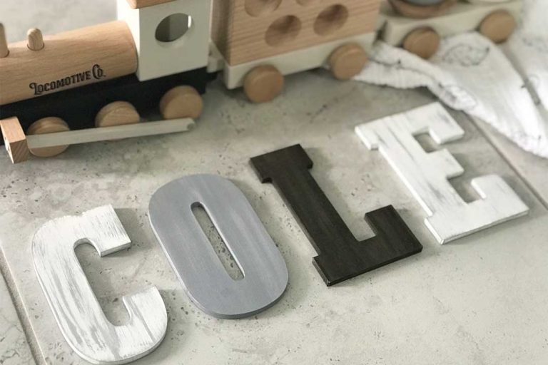 close up of white, gray, and brown painted and distressed wood letters laying on a tile floor with a wood train and muslin blanket