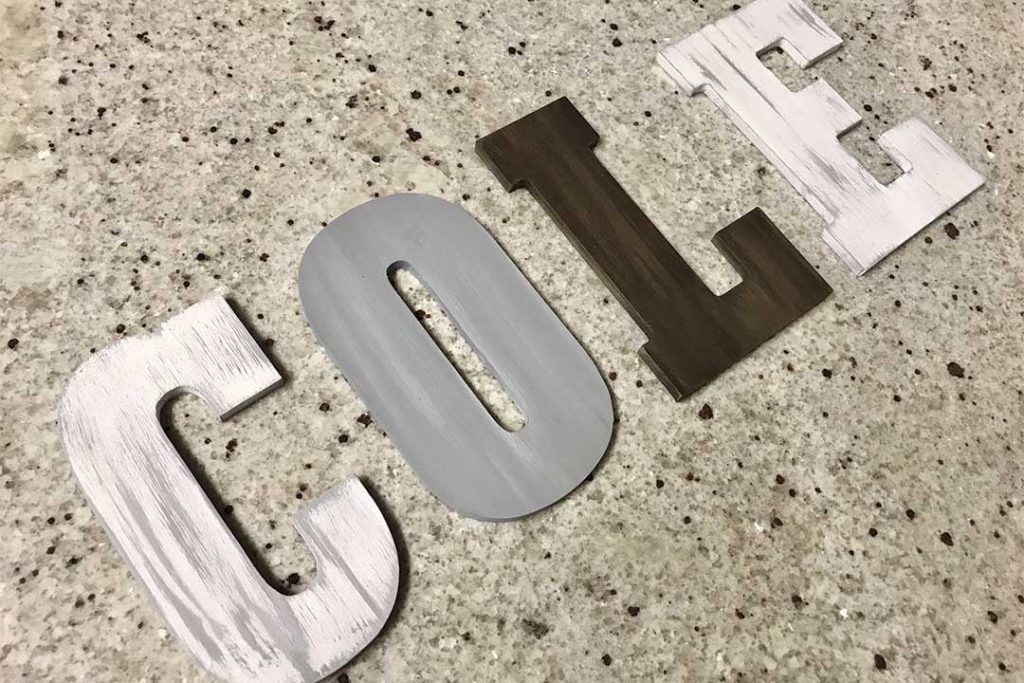 painted and distressed wood letters on a granite counter. white distressed with gray, gray distressed with white, and brown distressed with light brown