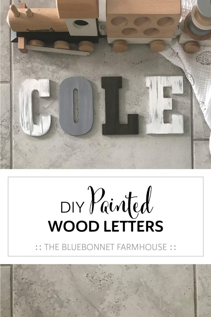 painted and distressed wood letters laying on a tile floor with a wood train and muslin blanket. Text reads "diy painted wood letters the bluebonnet farmhouse"
