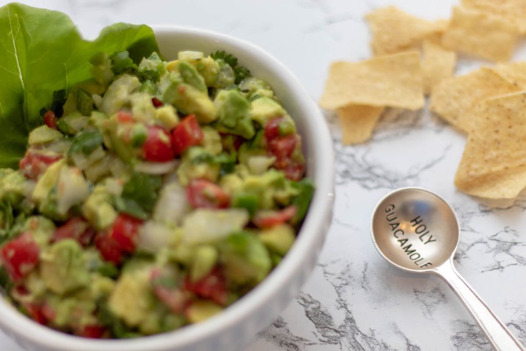 chunky tableside guacamole served in a guacamole serving bowl set with silver spoon that says, "holy guacamole"