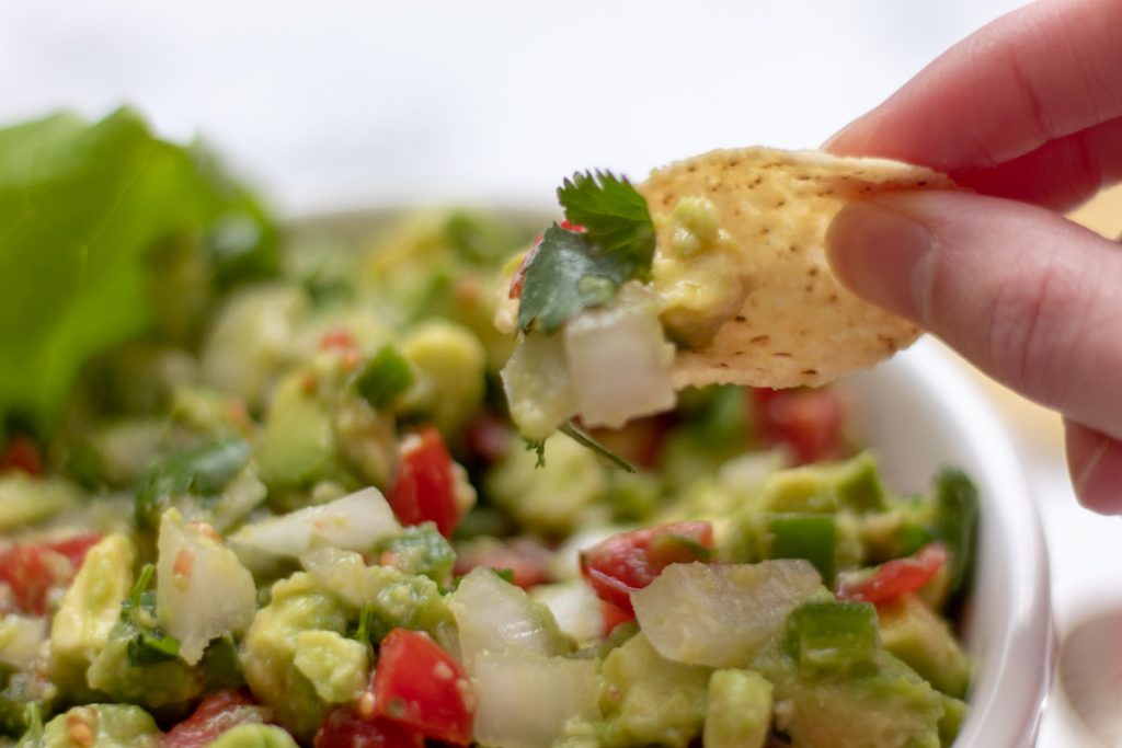 close up of chunky tableside guacamole scooped into an organic white corn tortilla chip