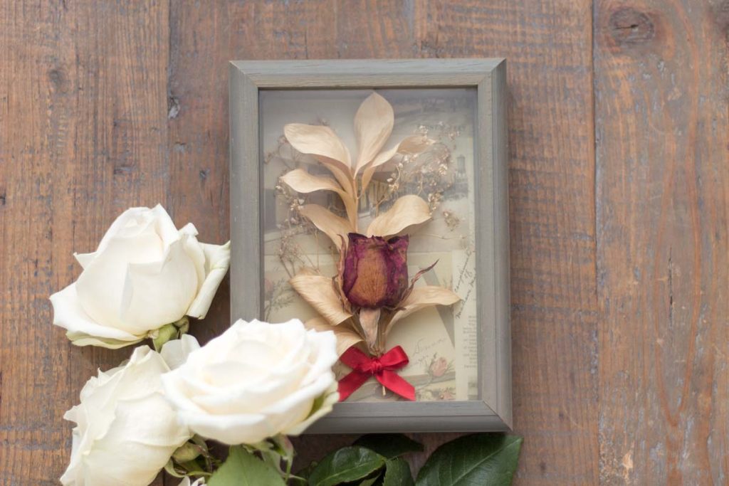 diy dried flower shadow box on a farmhouse table with three fresh white roses.