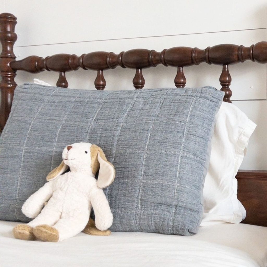 puppy organic stuffed animal on an antique jenny lind bed with muted blue and ivory bedding and white shiplap wall behind