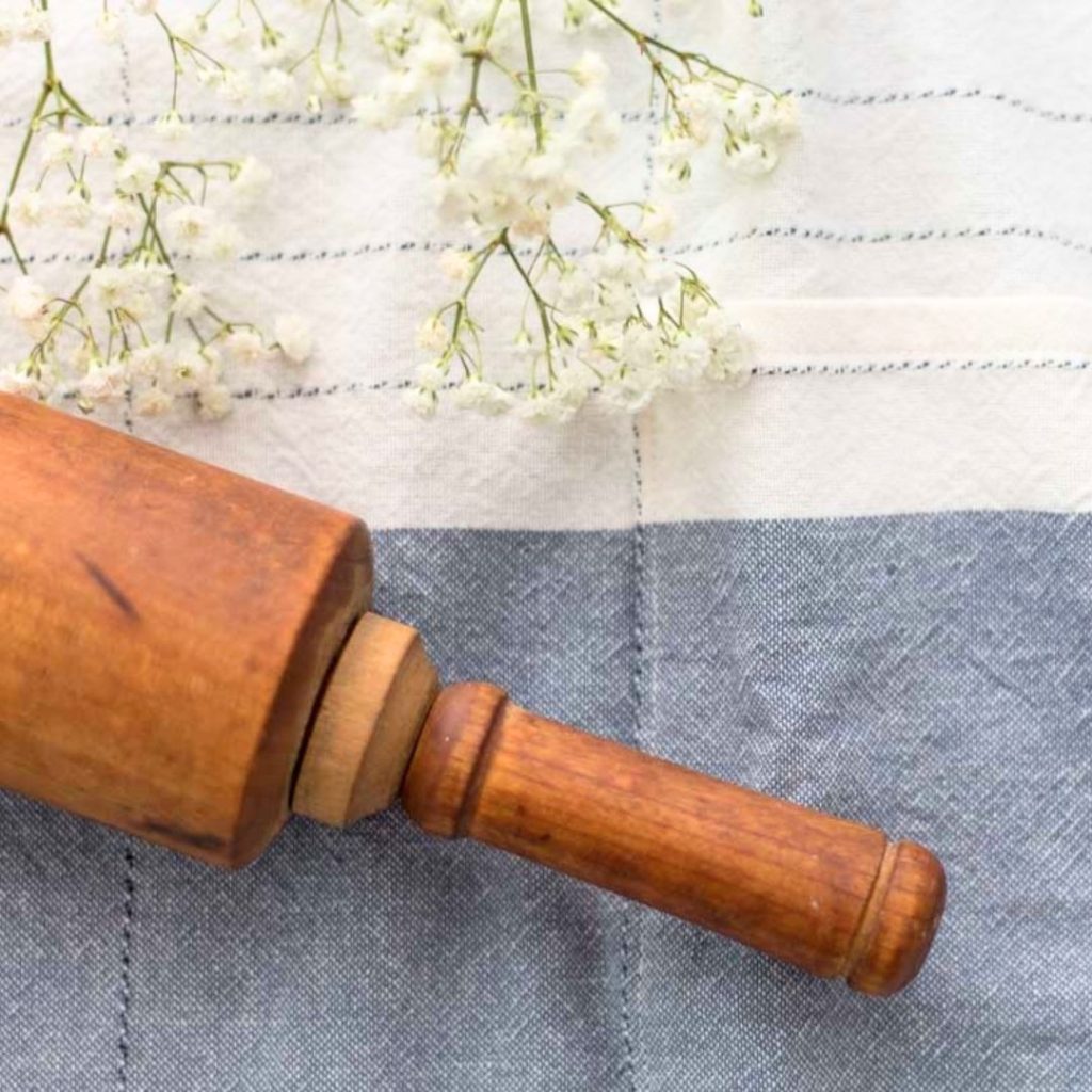 antique farmhouse rolling pin on blue and white cotton flour sack towel waist apron with white babies breath