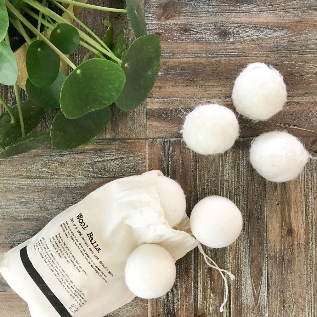 wool dryer balls for the laundry spilling out of a cotton draw string bag on a distressed wood surface with a pilea plant