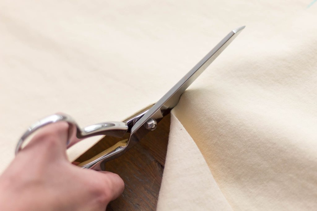 sewing shears cutting the fabric of a mattress protector into two pieces