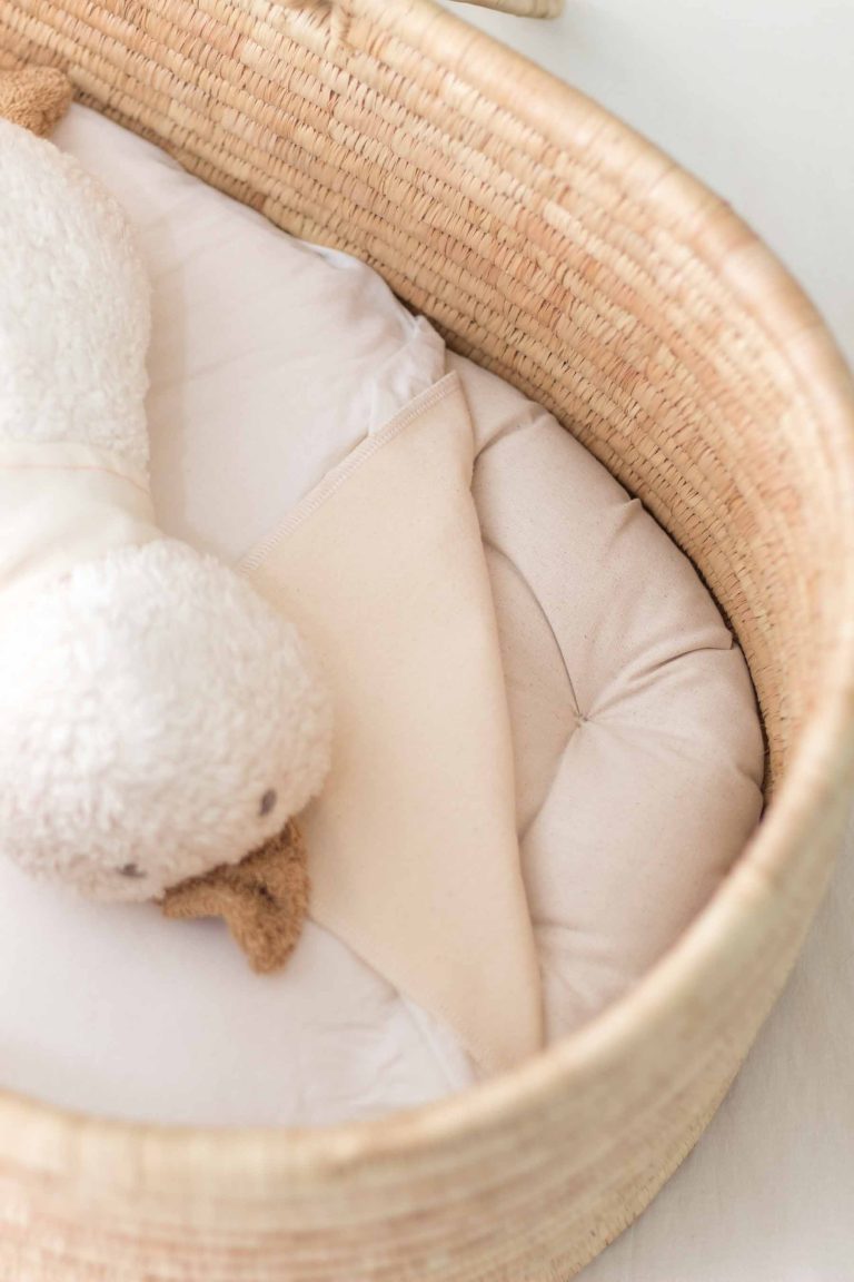 sisal grass and straw moses basket with mattress protector and sheet folded over to show organic kapuk bassinet mattress with organic stuffed animal duck on top