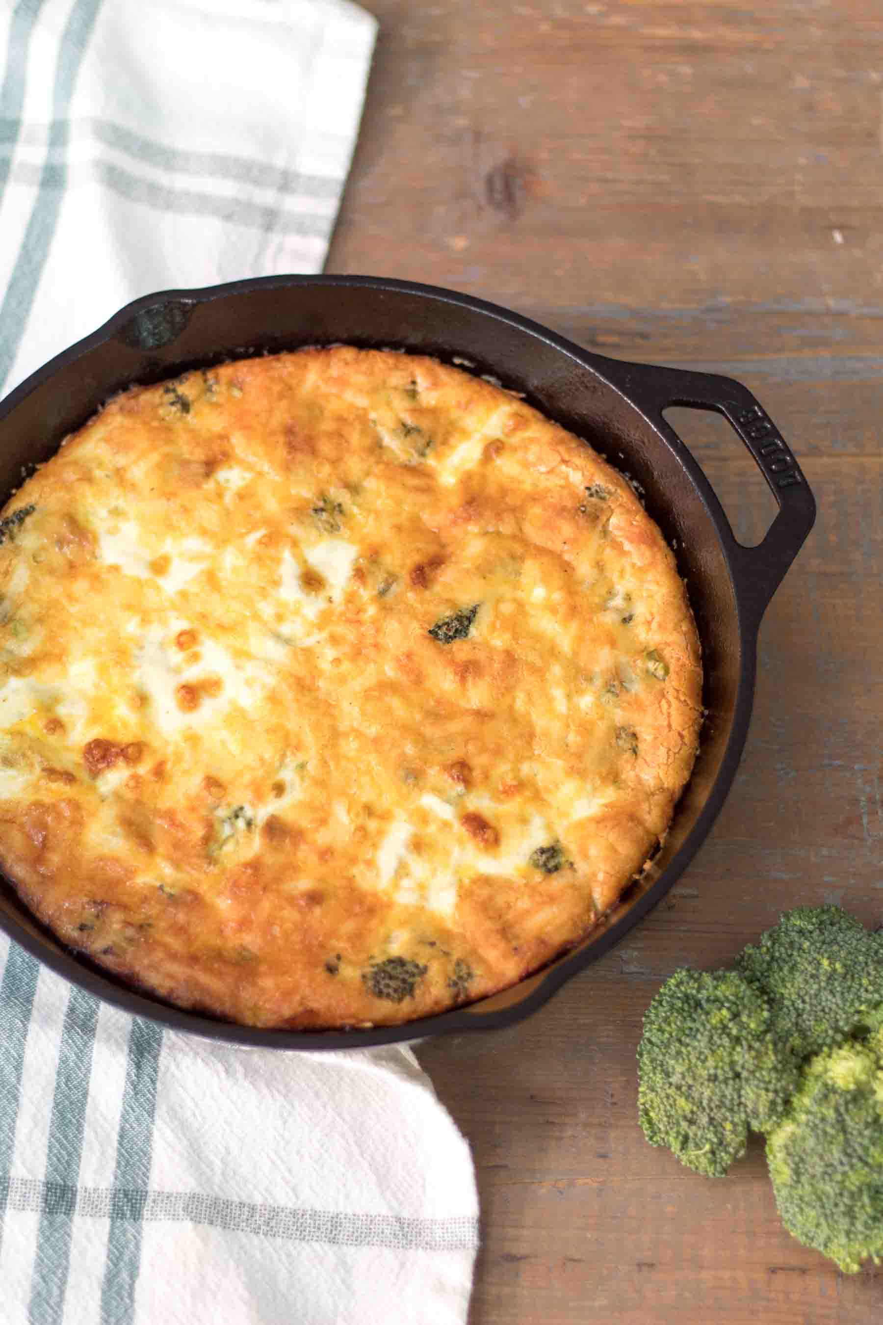 baked quiche in a cast iron skillet with broccoli florets on a farmhouse table