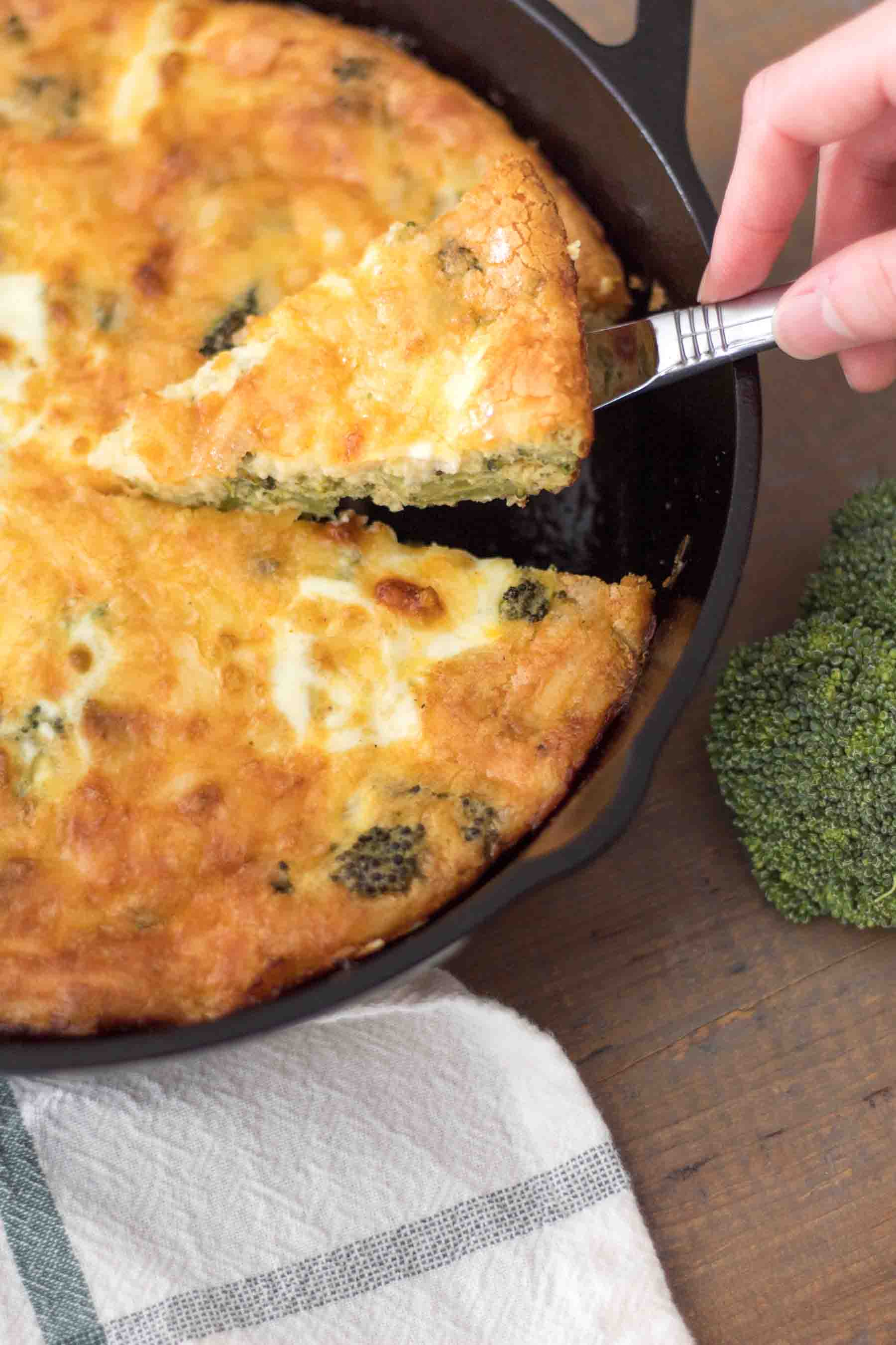 slice of crustless broccoli cheddar quiche being served out of a cast iron skillet
