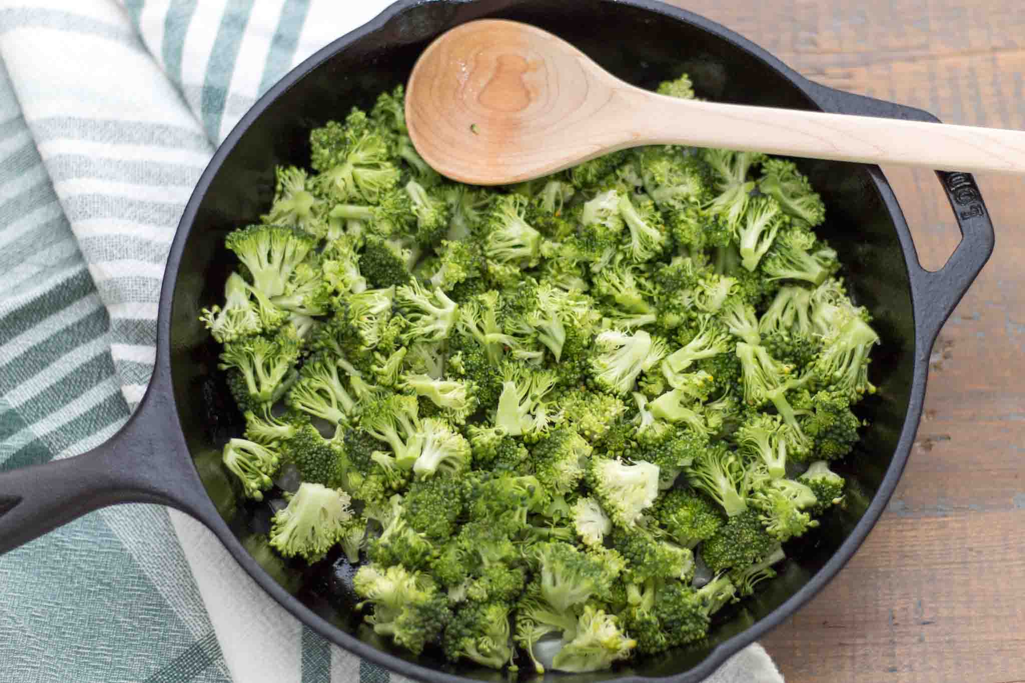 chopped broccoli florets in a cast iron skillet with a maple wood spoon