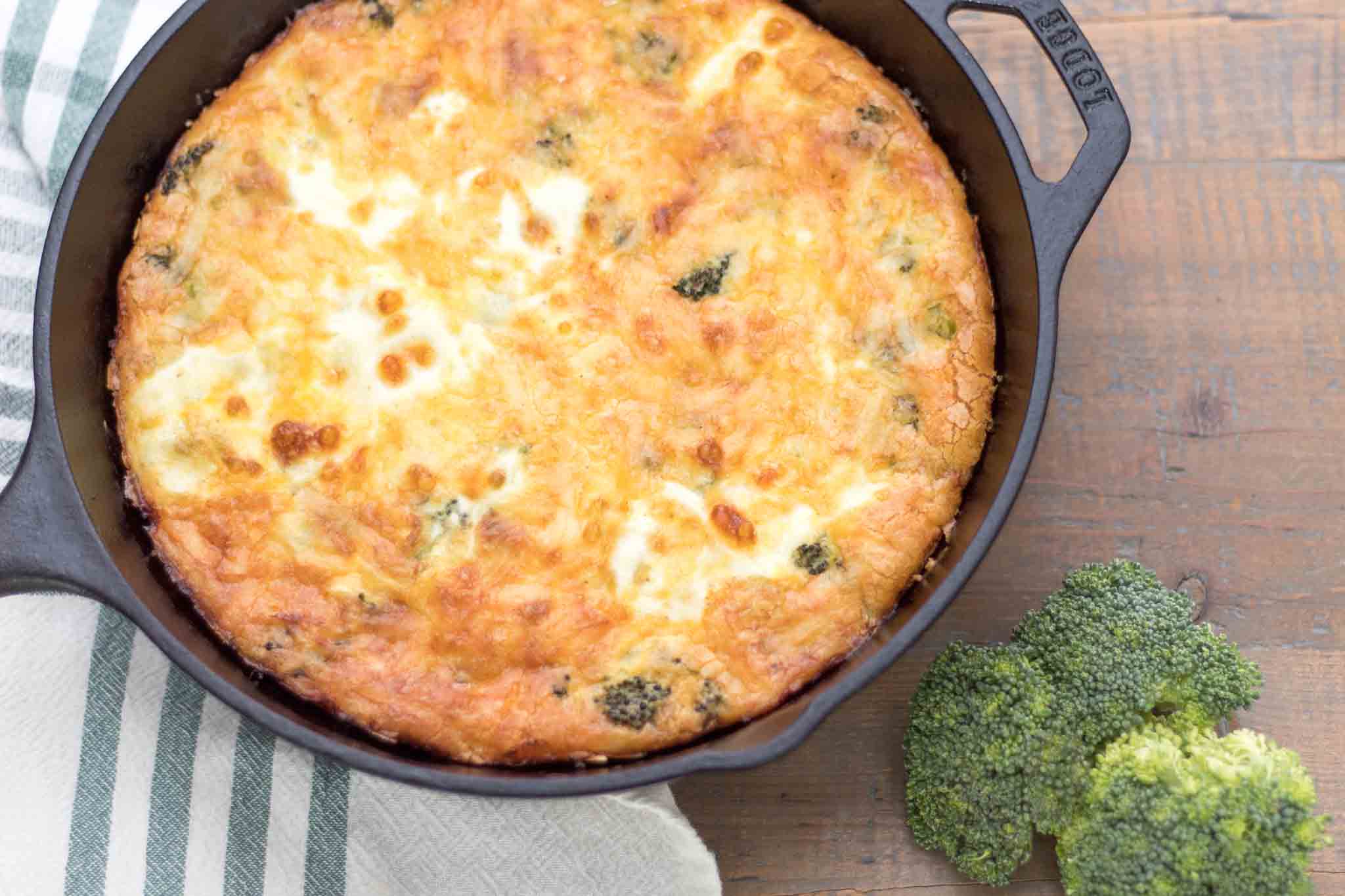 baked broccoli cheddar quiche in a cast iron skillet with broccoli florets on a farmhouse table