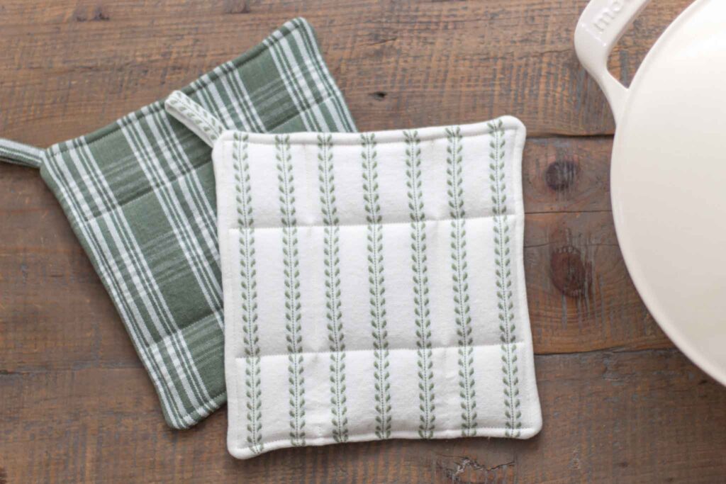 green and white handmade potholders next to an antique white enamel cast iron dutch oven on a farmouse table