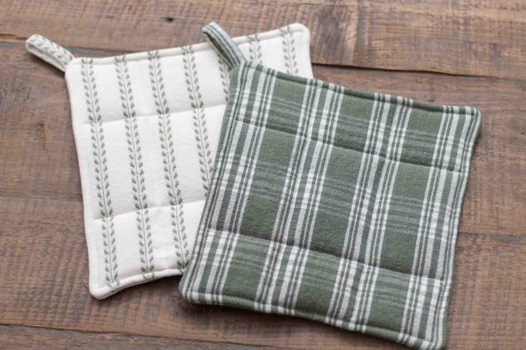 simple diy potholders made with cotton duck fabric. one fabric is green and white plaid, and the other fabric is white with embroidered green leafy vines in straight lines