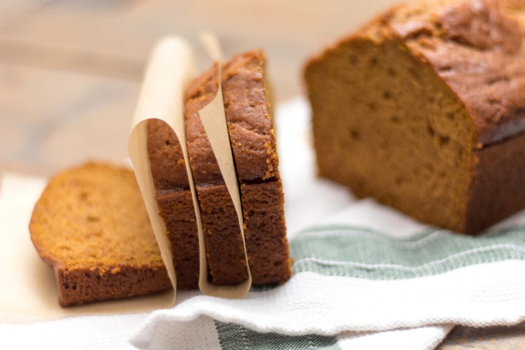 closeup of how to freeze pumpkin bread with slices divided by parchment paper and loaf in the background