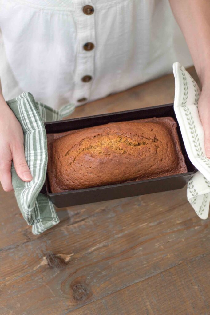 pumpkin bread in a cast iron loaf pan being held with green and white handmade potholders