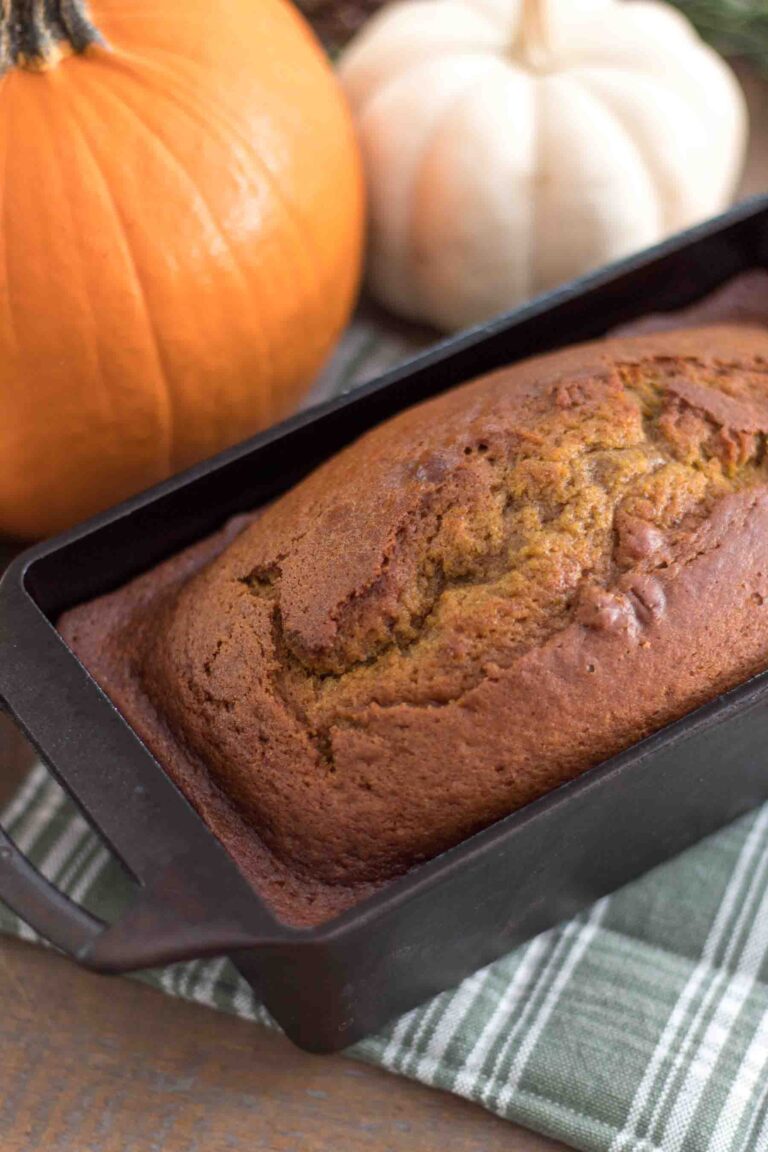 closeup of einkorn pumpkin bread in a cast iron loaf pan with orange and white pumpkins in the background