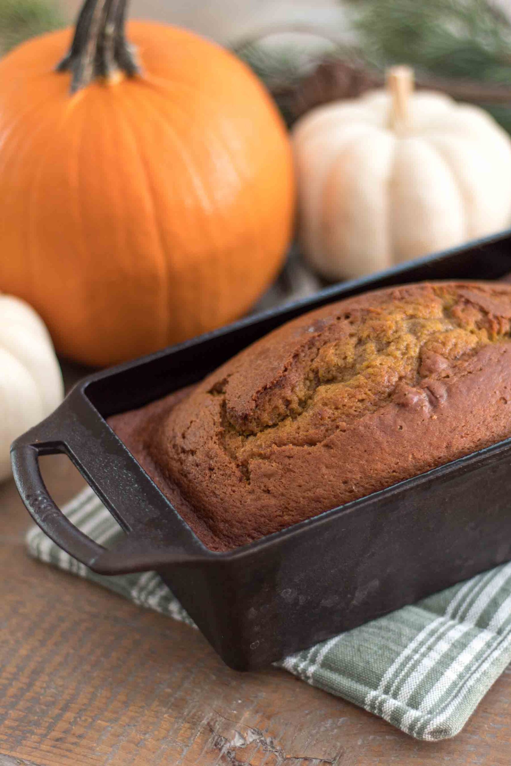 pumpkin bread with einkorn flour sitting on a green and white plaid handmade potholder with pumpkins and greenery in background