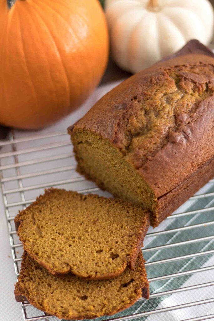 moist einkorn pumpkin bread loaf with slices on a cooling rack with orange and white pumpkins in the background