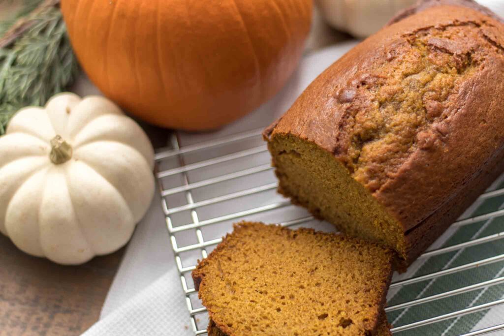 closeup of moist pumpkin bread slices with loaf on a cooling rack next to a small white pumpkin