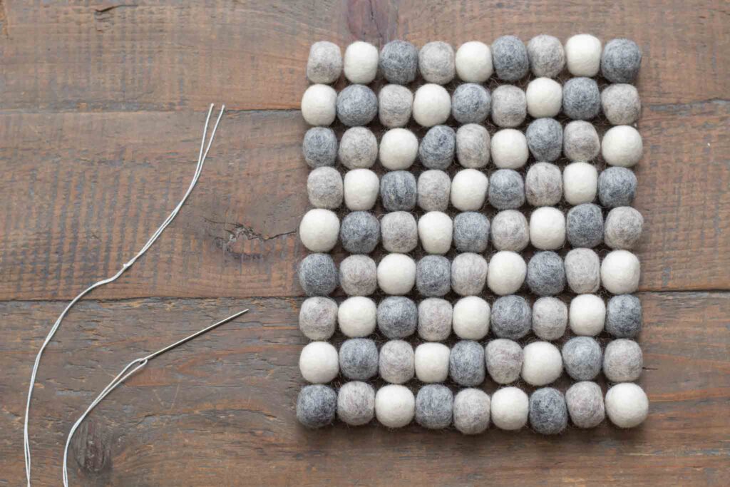 felt balls arranged in a nine by nine square next to a threaded yarn needle with a double knot and four inch tail