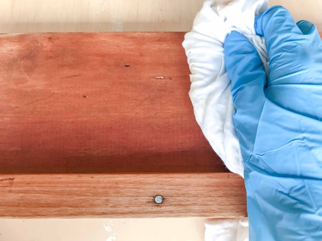 close-up photo of wiping away any excess wood conditioner with a lint free staining rag on antique bed side rails