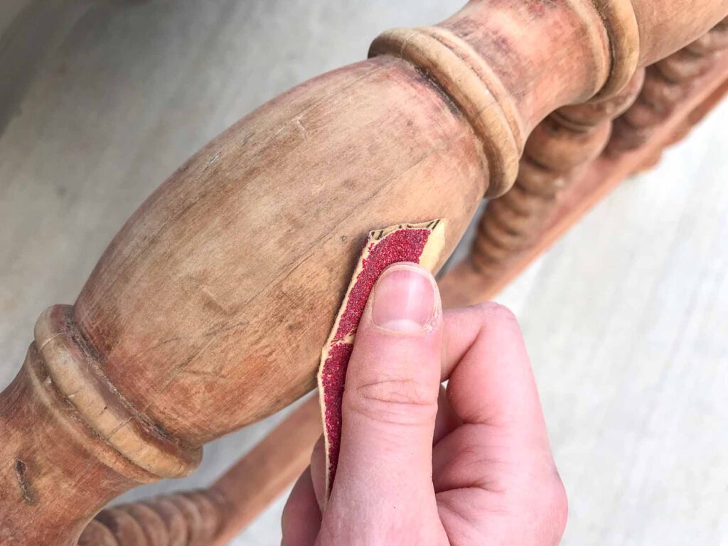 close-up view of hand sanding the spindles of an antique jenny lind bed to prep for staining