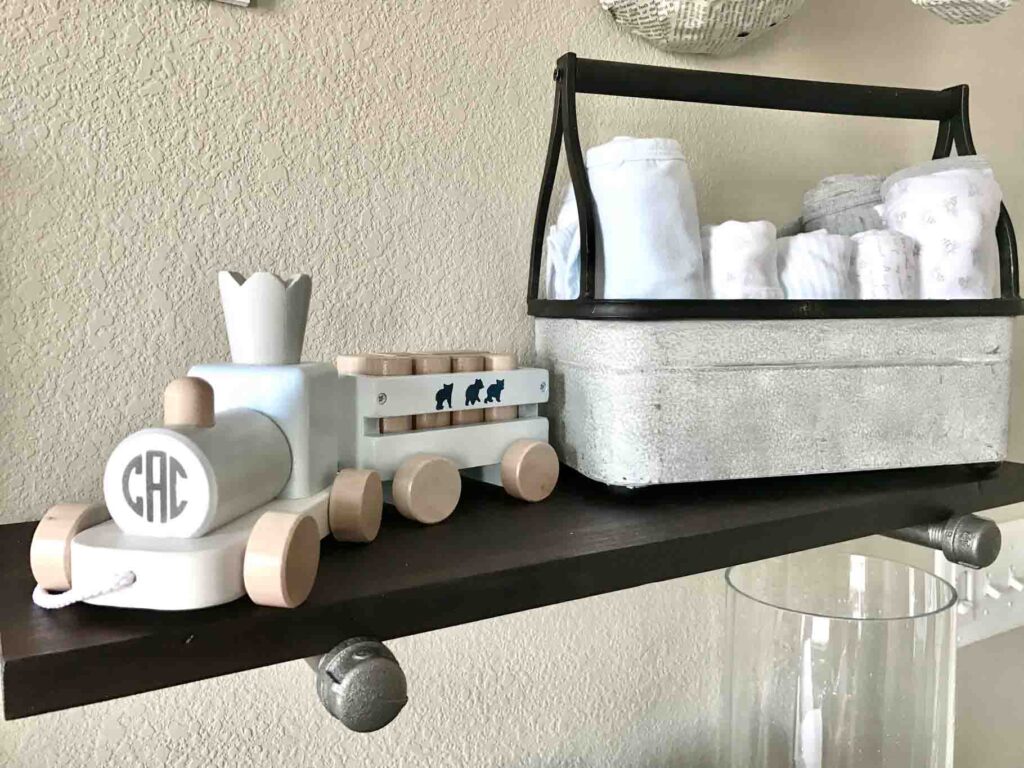 DIY industrial pipe shelf with baby bee burp clothes and blankets in a metal caddy next to a toy wood train.