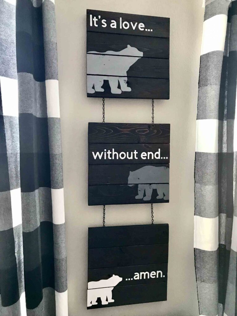 DIY woodland nursery wood signs with painted bears and the words "it's a love without end amen" framed by handmade black and white buffalo check curtains on each side