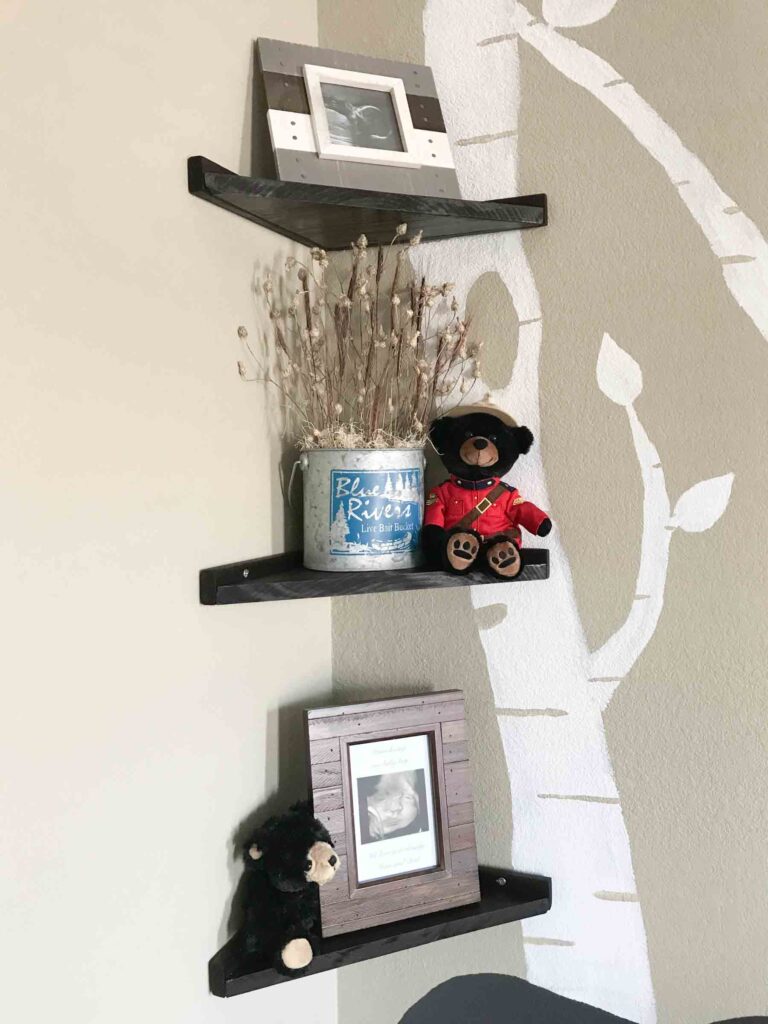 closeup of DIY floating corner shelves with picture frames, black bear stuffed animals, and white painted birch trees on the wall