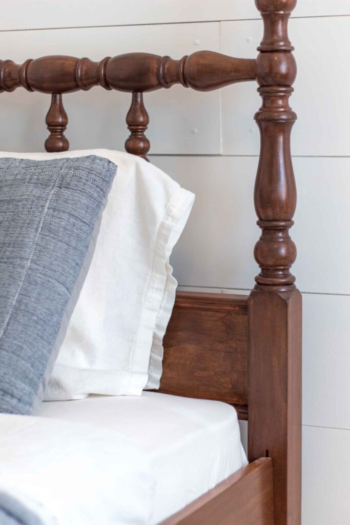 close-up of an antique jenny lind twin headboard in front of a white shiplap wall with dusty blue and ivory bedding