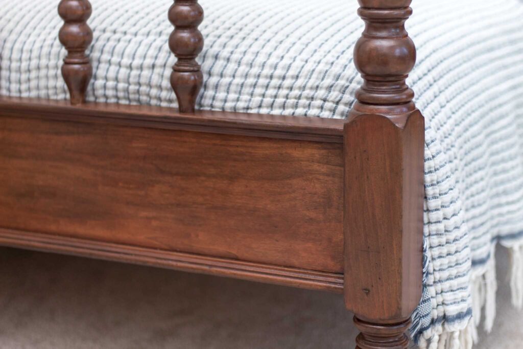 refinished antique jenny lind twin bed footboard in a medium brown stain with a blue and ivory muslin blanket at the foot of the bed