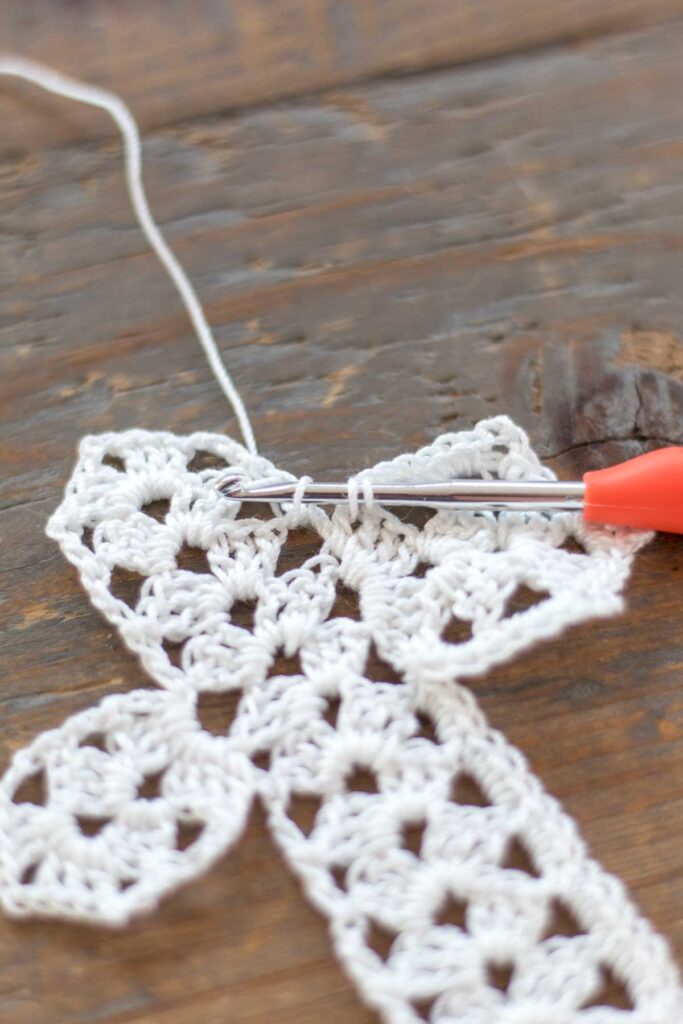 close-up of crochet hook pulling up the loops to create a single crochet two together at the corners of the cross