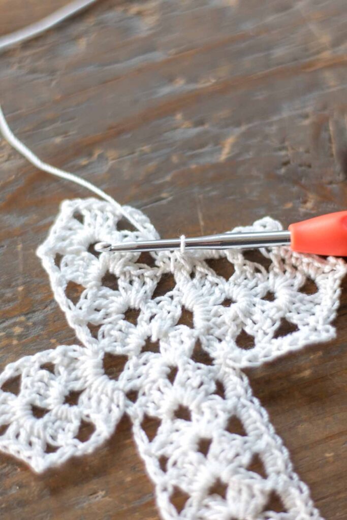 close-up of crochet hook holding the loop of the completed single crochet two together at the corners of the cross
