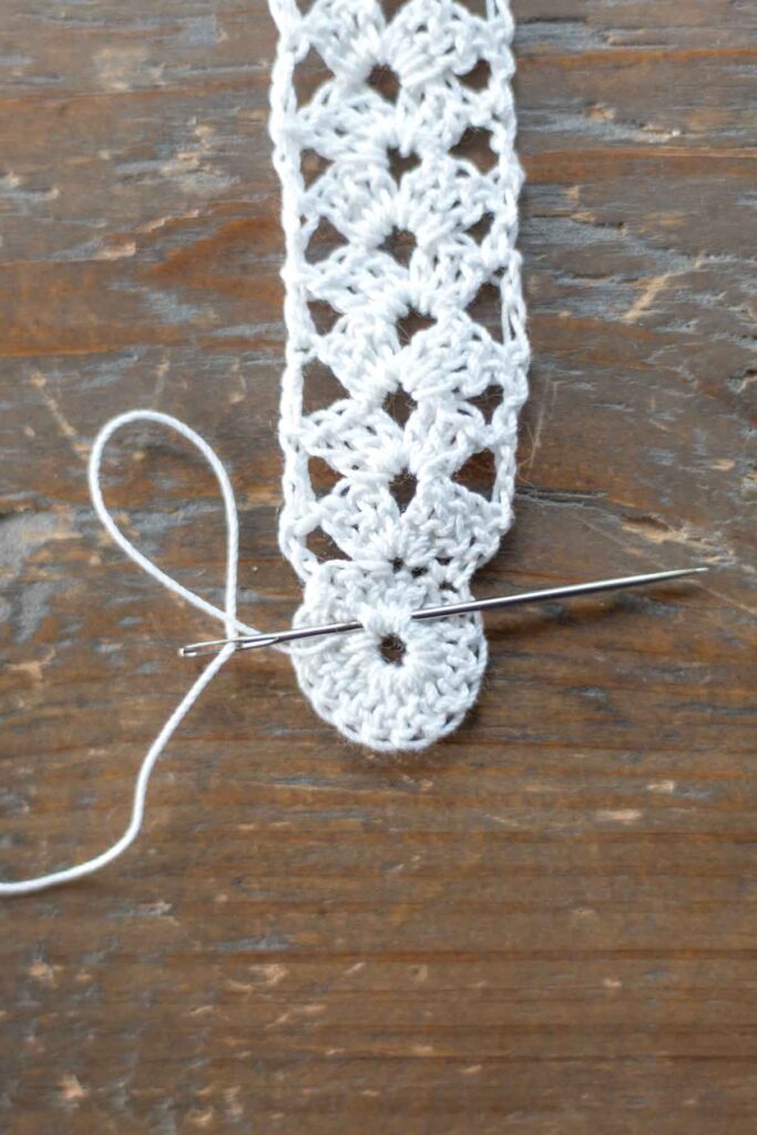close-up of yarn needle weaving loose end back into the round of crochet stitches