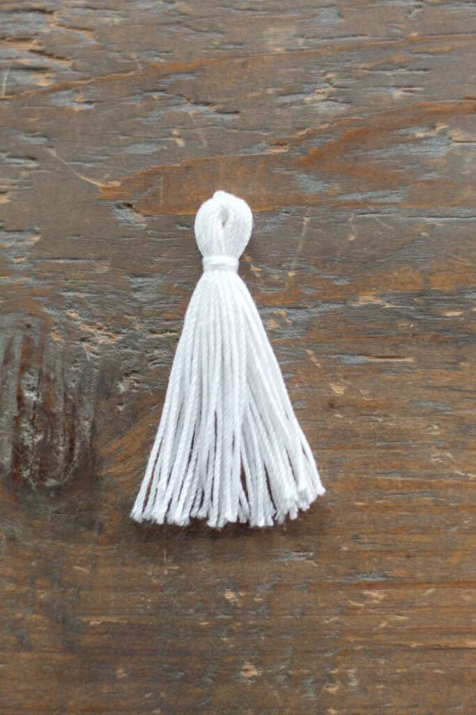 completed 2 inch white crochet thread tassel with a knot at the top and strand wrapped around the tassel about 1/4 of an inch down from the top