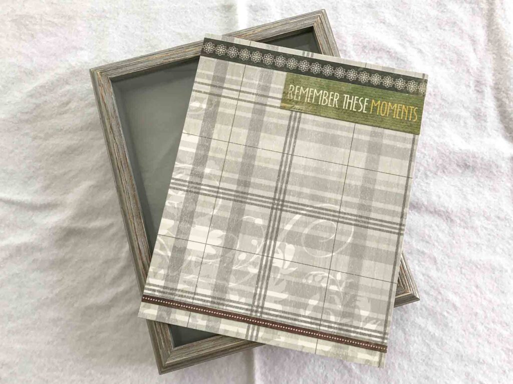 decorative neutral plaid scrapbook paper and floral trim on the back panel of a shadow box. decorative text reads "remember these moments"