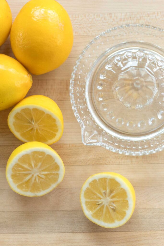 glass citrus reamer with whole lemons and lemons cut in half on a maple wood cutting board