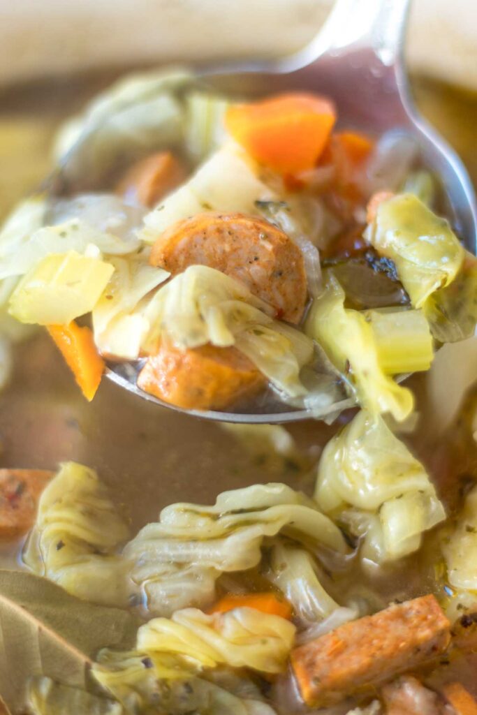 close up of a ladle filled with sausage, cabbage, and potato soup