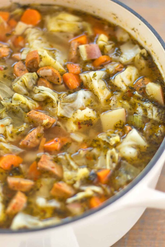 close up of an antique white dutch oven filled with sausage, cabbage, and potato soup