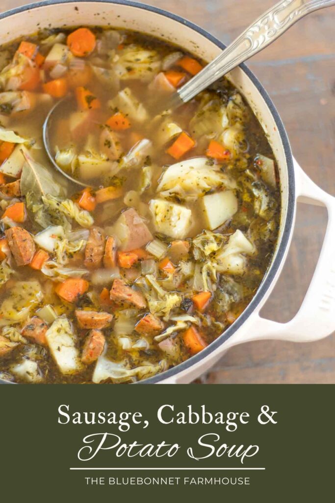 dutch oven full of sausage, cabbage, and potato soup with a vintage ladle and blue striped tea towel on a farmhouse wood table. text reads "sausage, cabbage, and potato soup - the bluebonnet farmhouse"