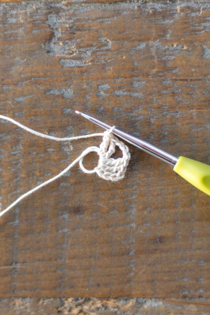 magic ring with a total of 5 triple crochet stitches and 3 chain stitches in white crochet thread with hook at end of the row to begin the right arm of the cross bookmark