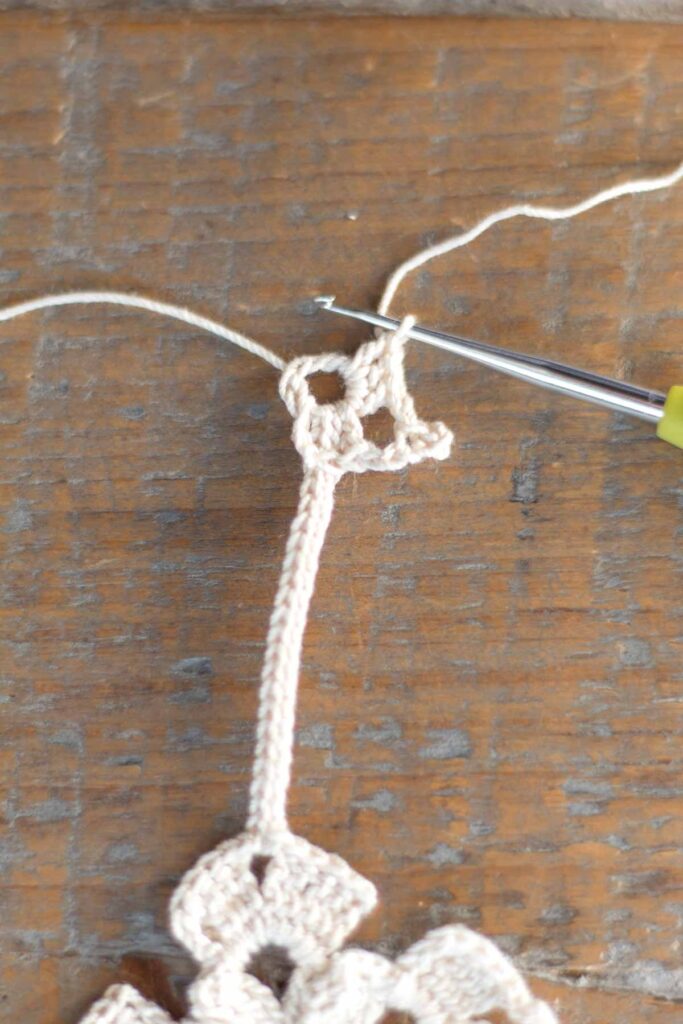 working around the cross bookmark loop to form the crochet star with clusters of 3 double crochet stitches, chain stitches, and slip stitches