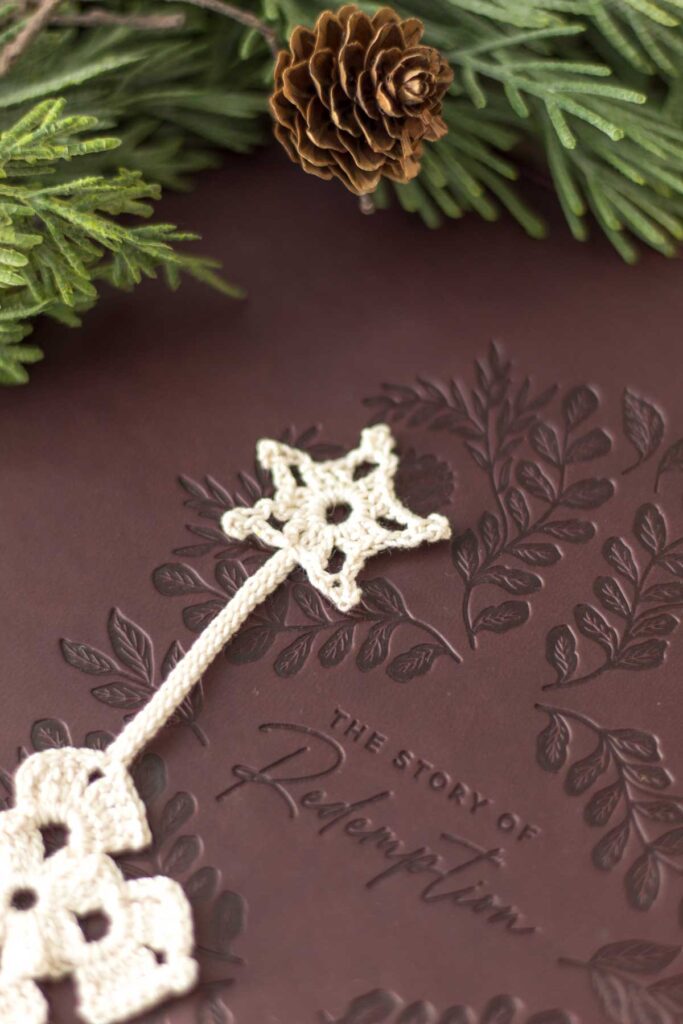 closeup of an antique white crochet thread Christmas star at the top of a cross bookmark lying on a dark brown leather bible with cedar greenery and a small pine cone next to it